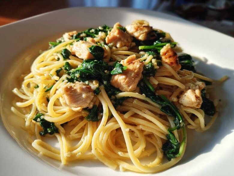 A close-up of a white plate filled with Garlic Butter Pasta with Chicken and Spinach, glistening under natural light.