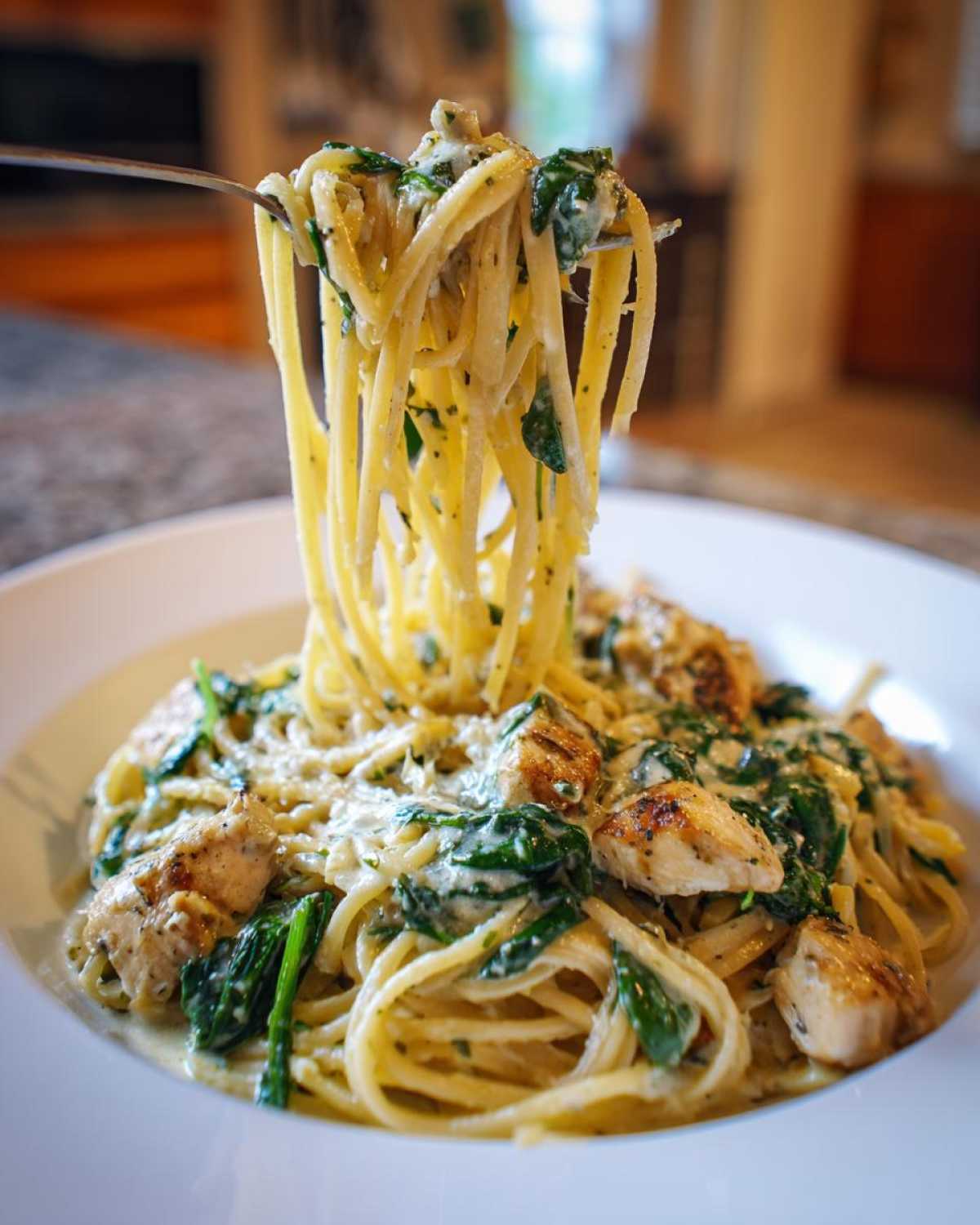A fork lifting spaghetti coated in creamy sauce, chicken, and spinach from a bowl of Garlic Butter Pasta with Chicken and Spinach.