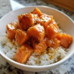Close-up of Garlic Butter Salmon Bites glazed in sauce and sprinkled with herbs, served over white rice in a bowl.