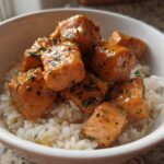 Close-up of glossy Garlic Butter Salmon Bites piled high on a bed of fluffy white rice in a white bowl.