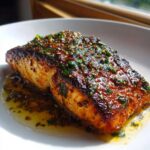 A perfectly cooked fillet of Garlic Butter Salmon with Crispy Skin Recipe, topped with glistening herbs and butter sauce.