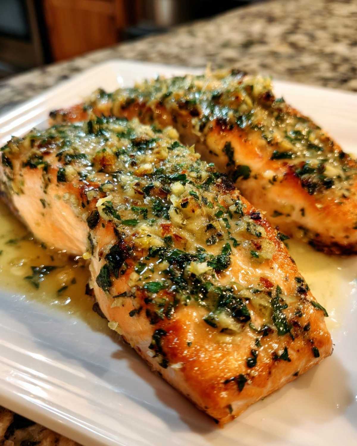 Two fillets of perfectly cooked Garlic Butter Salmon with Lemon Herb Sauce glistening on a white plate.