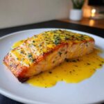A perfectly cooked fillet of Garlic Butter Salmon generously topped with bright yellow lemon garlic sauce and fresh parsley.