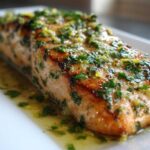 Close-up of a perfectly cooked fillet of Garlic Butter Salmon with Lemon Herb Sauce glistening on a white plate.