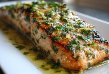 Close-up of a perfectly cooked fillet of Garlic Butter Salmon with Lemon Herb Sauce glistening on a white plate.