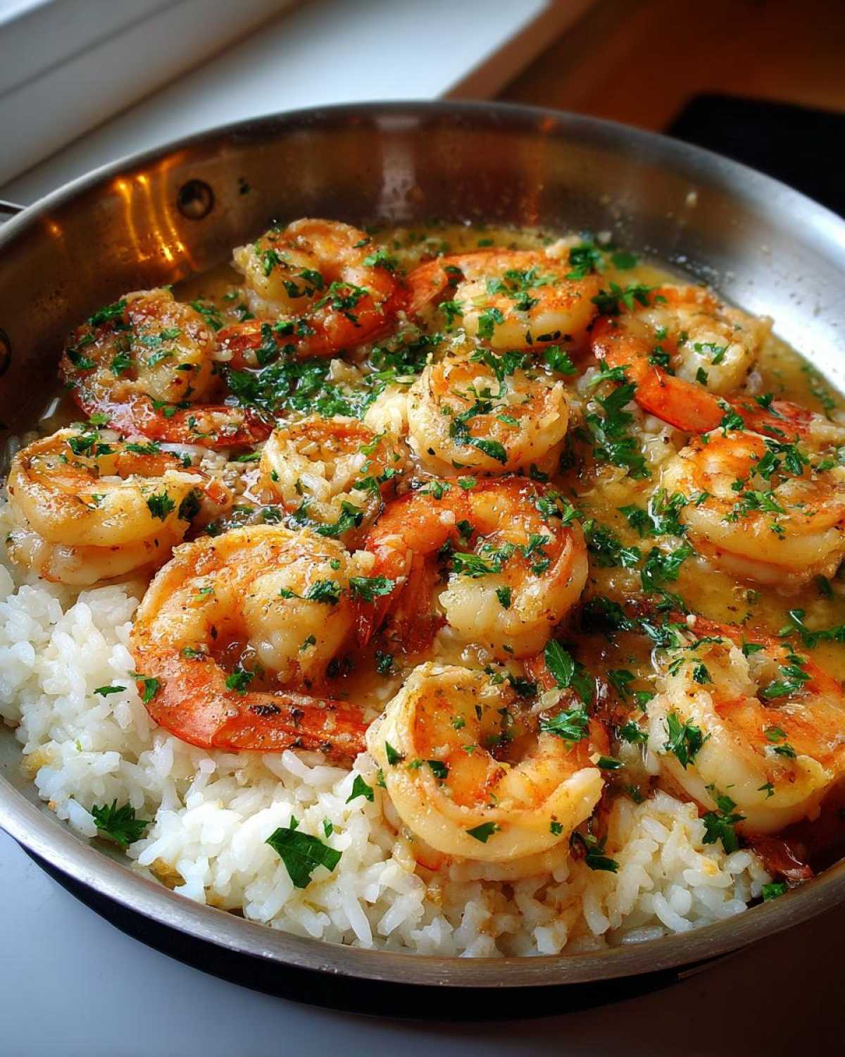 Close-up of plump shrimp coated in garlic butter sauce served over white rice in a stainless steel skillet.
