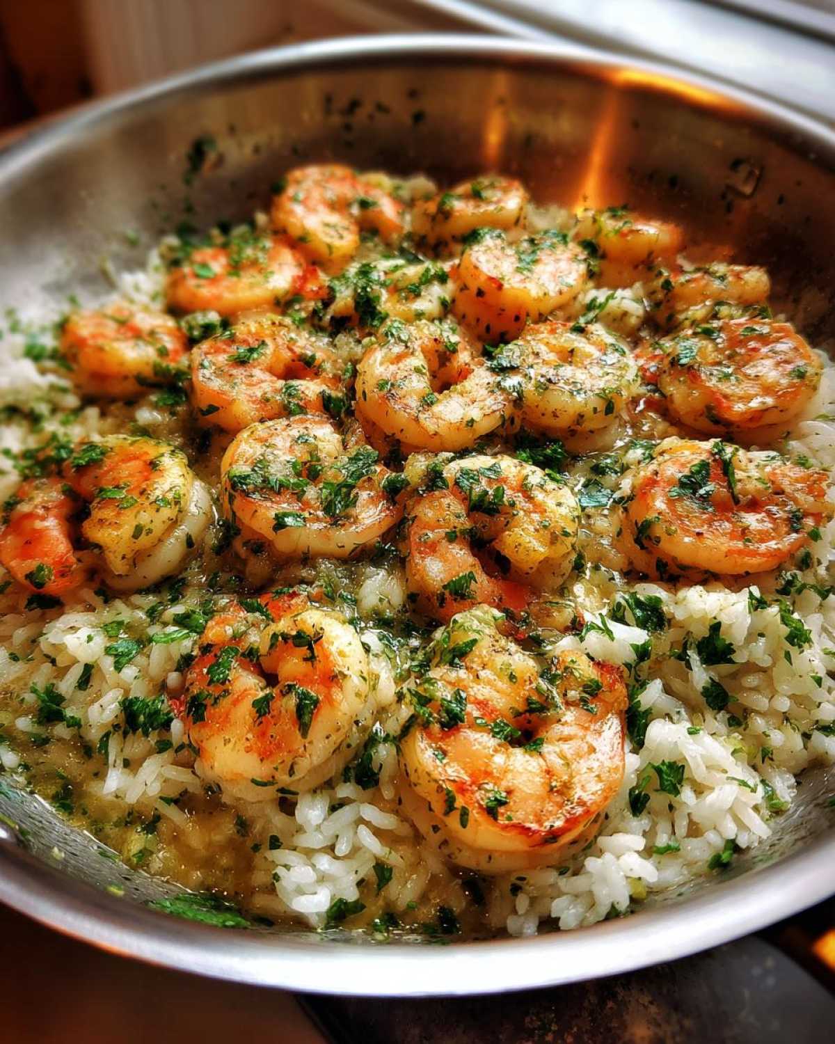 Close-up of juicy shrimp coated in garlic butter sauce served over white rice in a skillet, garnished with parsley.