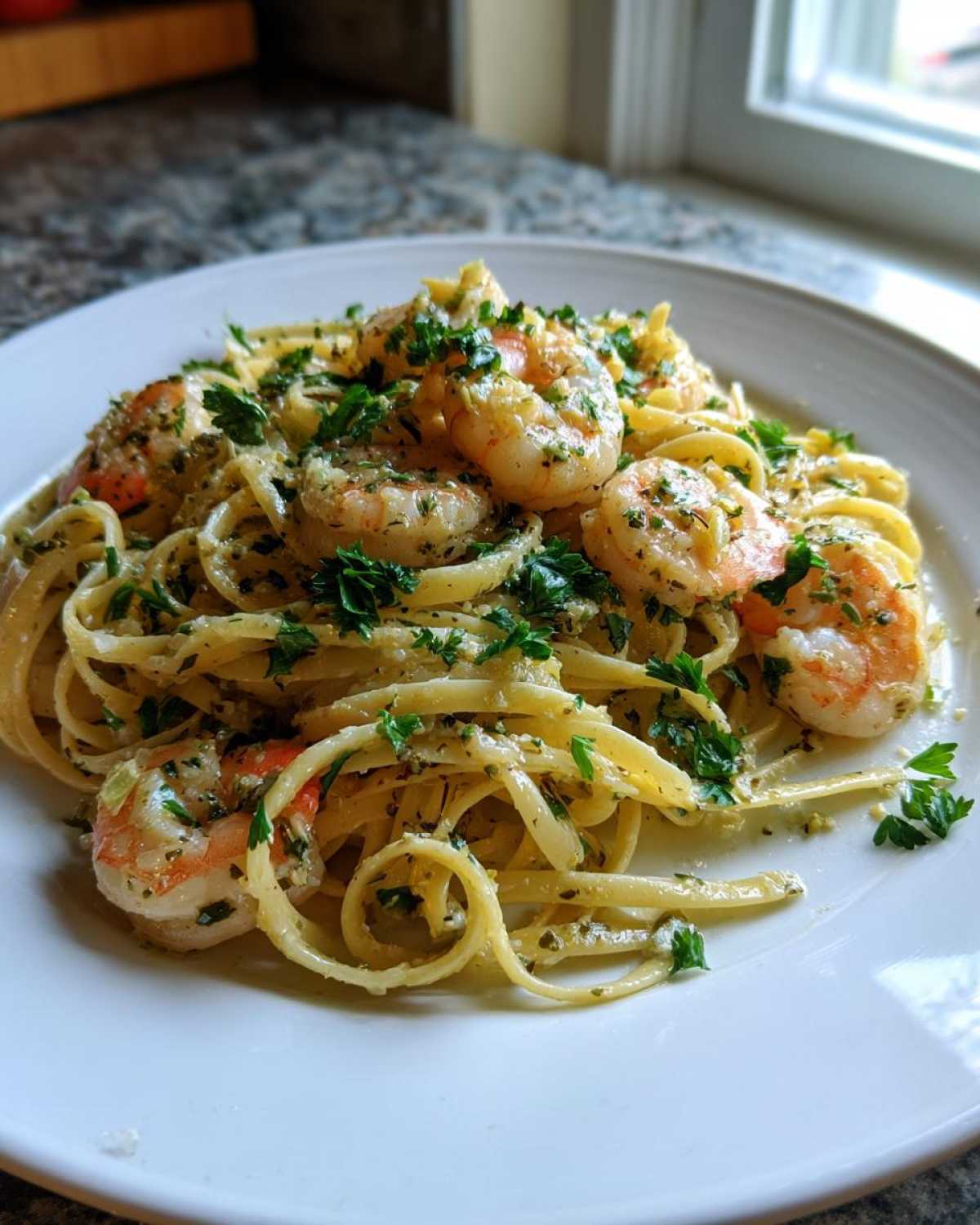 A close-up of a white plate filled with Garlic Butter Shrimp Pasta with Lemon Flavor, topped generously with fresh parsley.