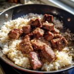 Close-up of seared steak cubes served over fluffy white rice in a black skillet, highlighting the Garlic Butter Steak and Rice Skillet Dinner.