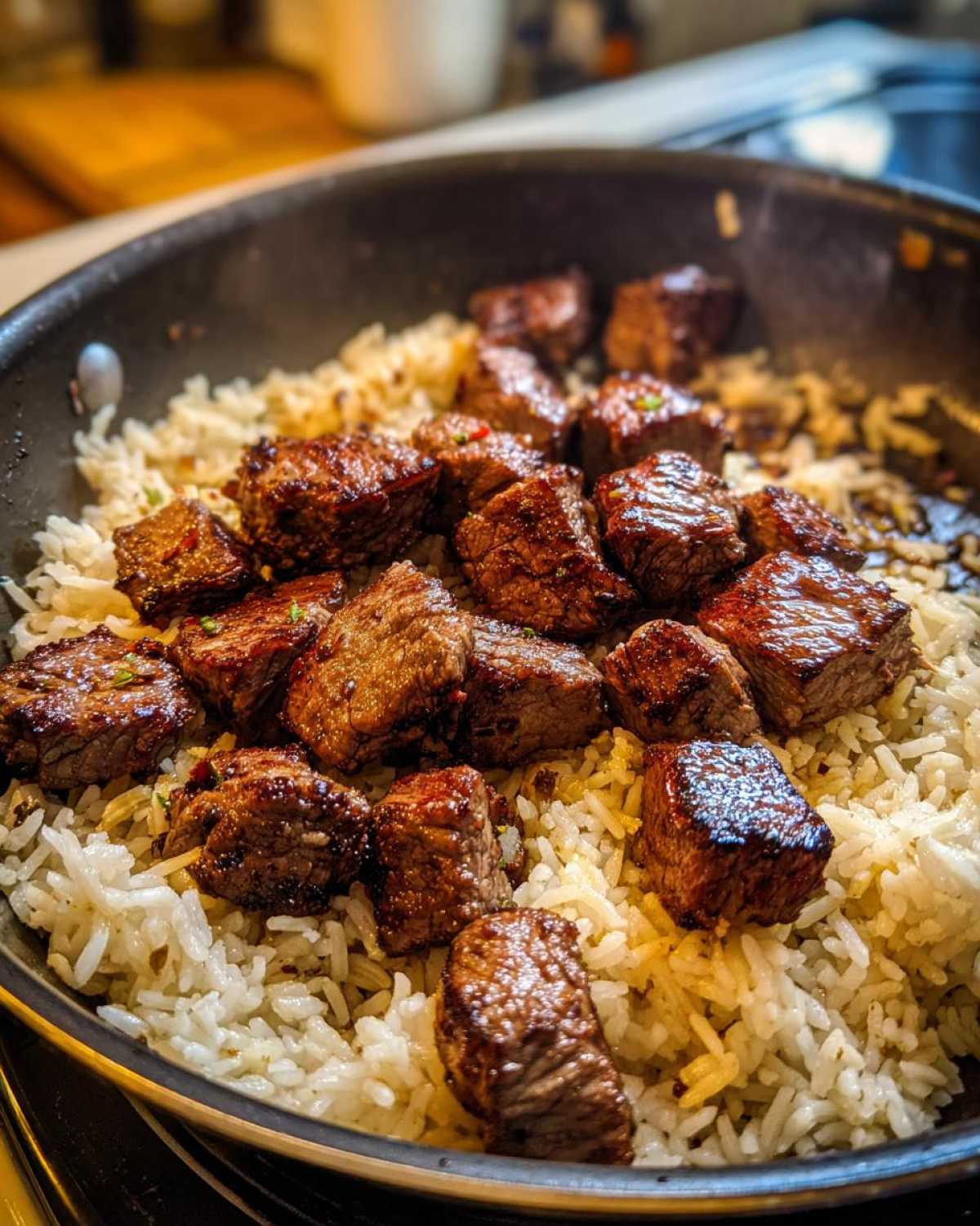 Close-up of seared steak bites served over fluffy white rice in a dark skillet for a Garlic Butter Steak and Rice Skillet Dinner.