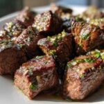 Close-up of perfectly seared Garlic Butter Steak Bites glistening with sauce and herbs on a white plate.