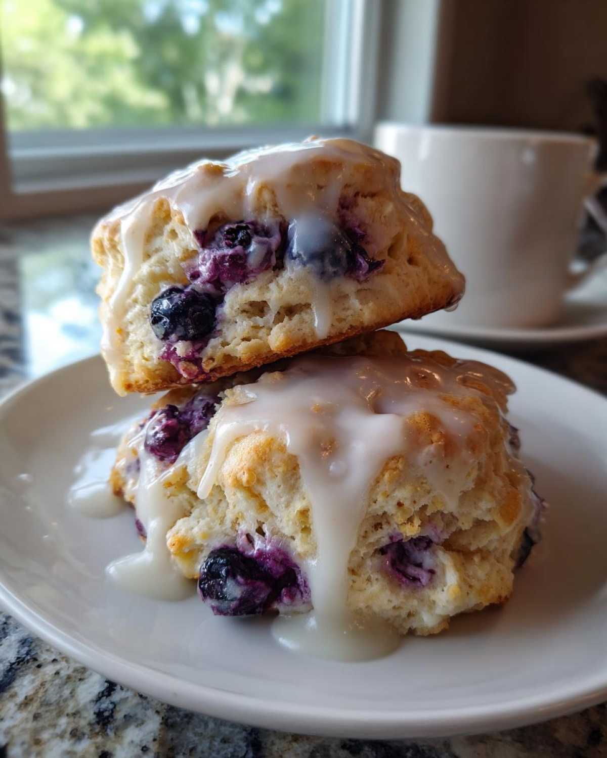 Two stacked Blueberry Lemon Scones drizzled with thick white glaze, served on a white plate.