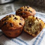 Three freshly baked Gluten-Free Banana Chocolate Chip Muffins, one cut open to show the moist interior.