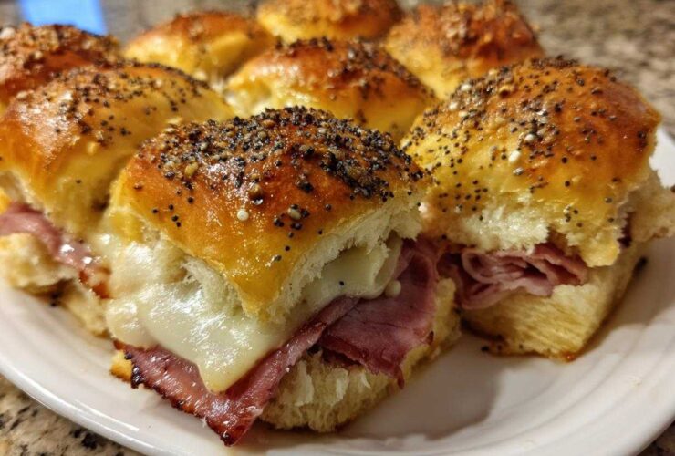 Close-up of baked Hawaiian Roll Ham and Cheese Sliders topped with poppy seeds and melted cheese.