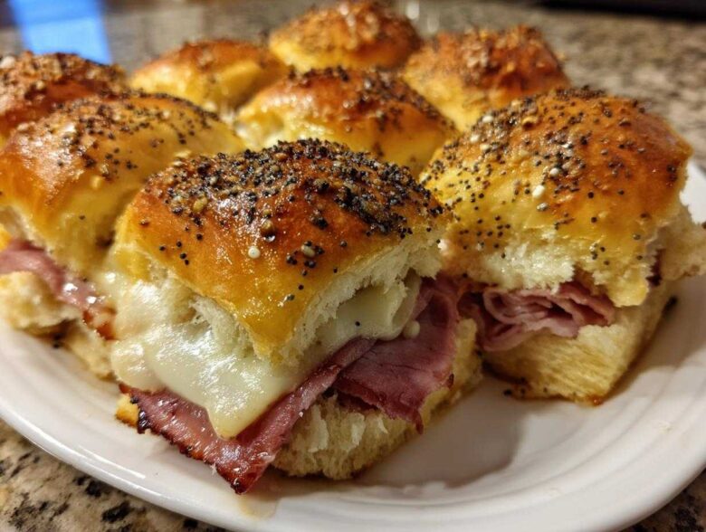 Close-up of baked Hawaiian Roll Ham and Cheese Sliders topped with poppy seeds and melted cheese.