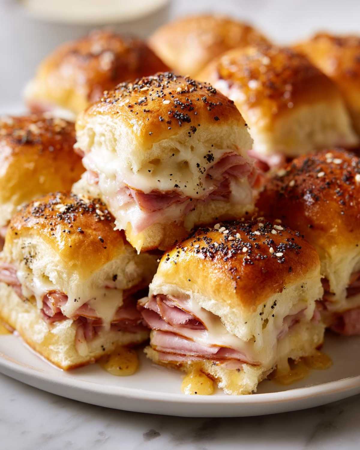 Close-up of Hawaiian Roll Ham and Cheese Sliders stacked, featuring melted Swiss cheese and a poppy seed glaze.