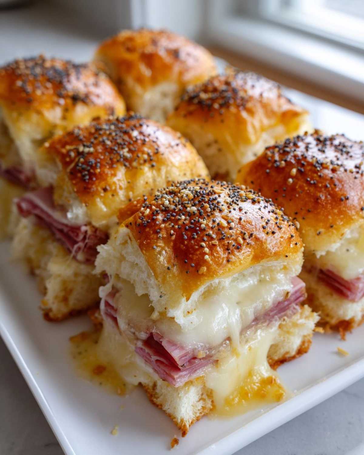 Close-up of baked Hawaiian Roll Ham and Cheese Sliders with melted Swiss cheese oozing out.