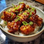 Close-up of a Honey Garlic Chicken Bowl with rice, topped with sticky glazed chicken, sesame seeds, and sliced green onions.
