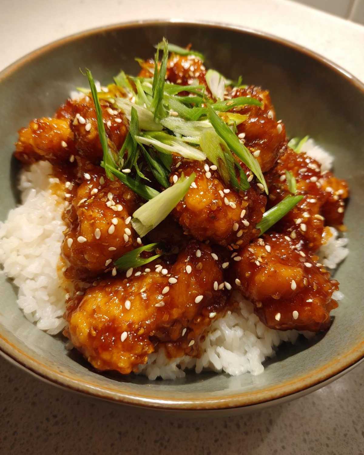 Close-up of a Honey Garlic Chicken Bowl with rice, topped with sesame seeds and sliced green onions.