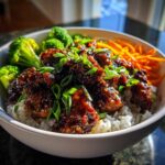 Close-up of a Honey Garlic Chicken Bowl featuring sticky glazed chicken pieces over white rice, broccoli, and shredded carrots.