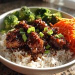 A close-up of a Honey Garlic Chicken Bowl featuring sticky glazed chicken pieces over white rice, served with steamed broccoli and shredded carrots.