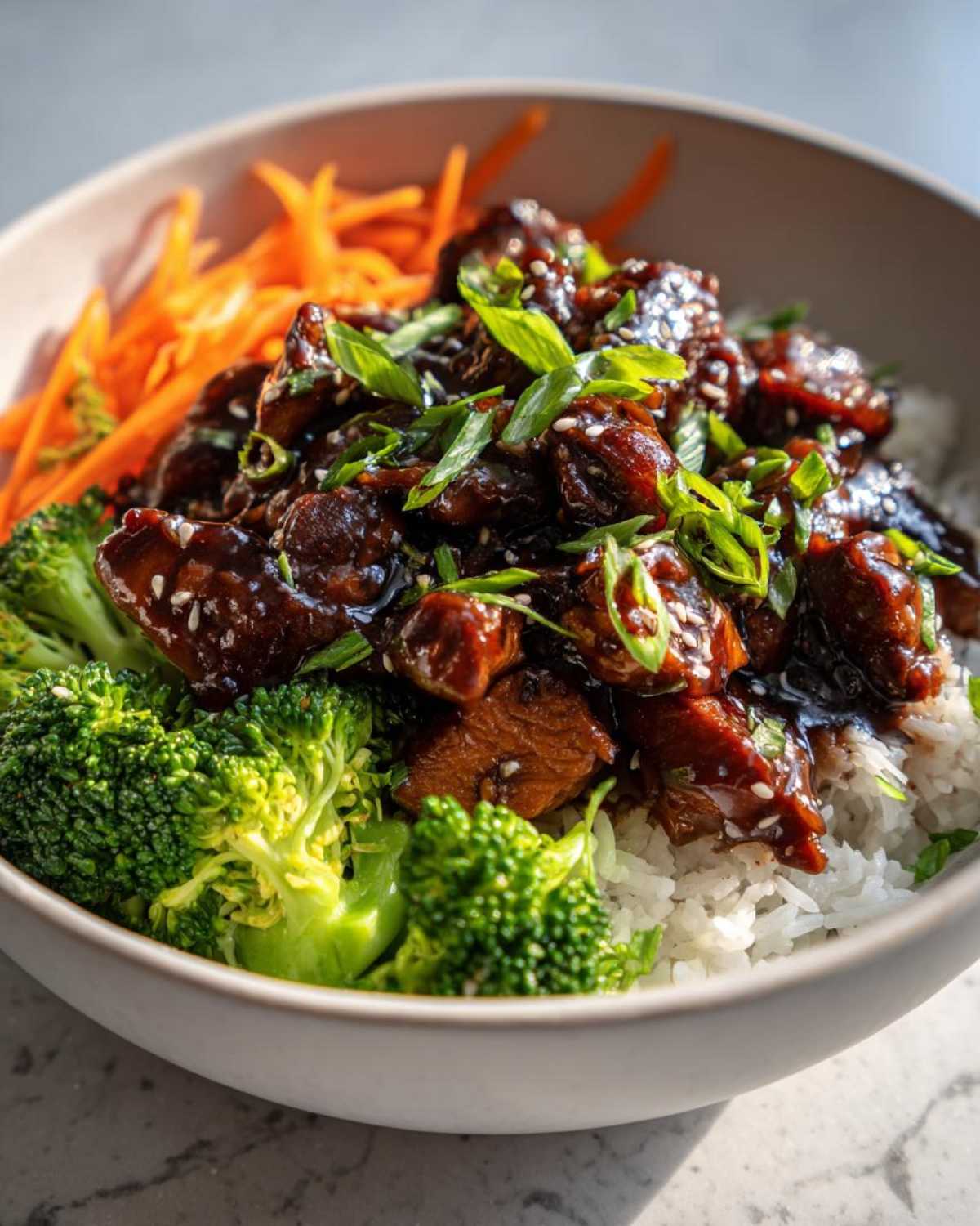 Close-up of a Honey Garlic Chicken Bowl featuring glazed chicken pieces over rice with bright green broccoli florets and shredded carrots.