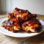 A stack of perfectly cooked Honey Garlic Chicken Thighs Oven Baked with a dark, shiny glaze on a white plate.