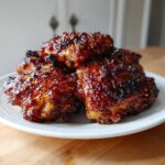 A stack of glistening, caramelized Honey Garlic Chicken Thighs Oven Baked served on a white plate.