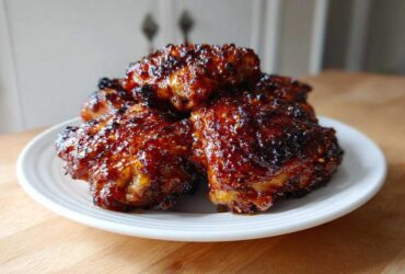 A stack of glistening, caramelized Honey Garlic Chicken Thighs Oven Baked served on a white plate.