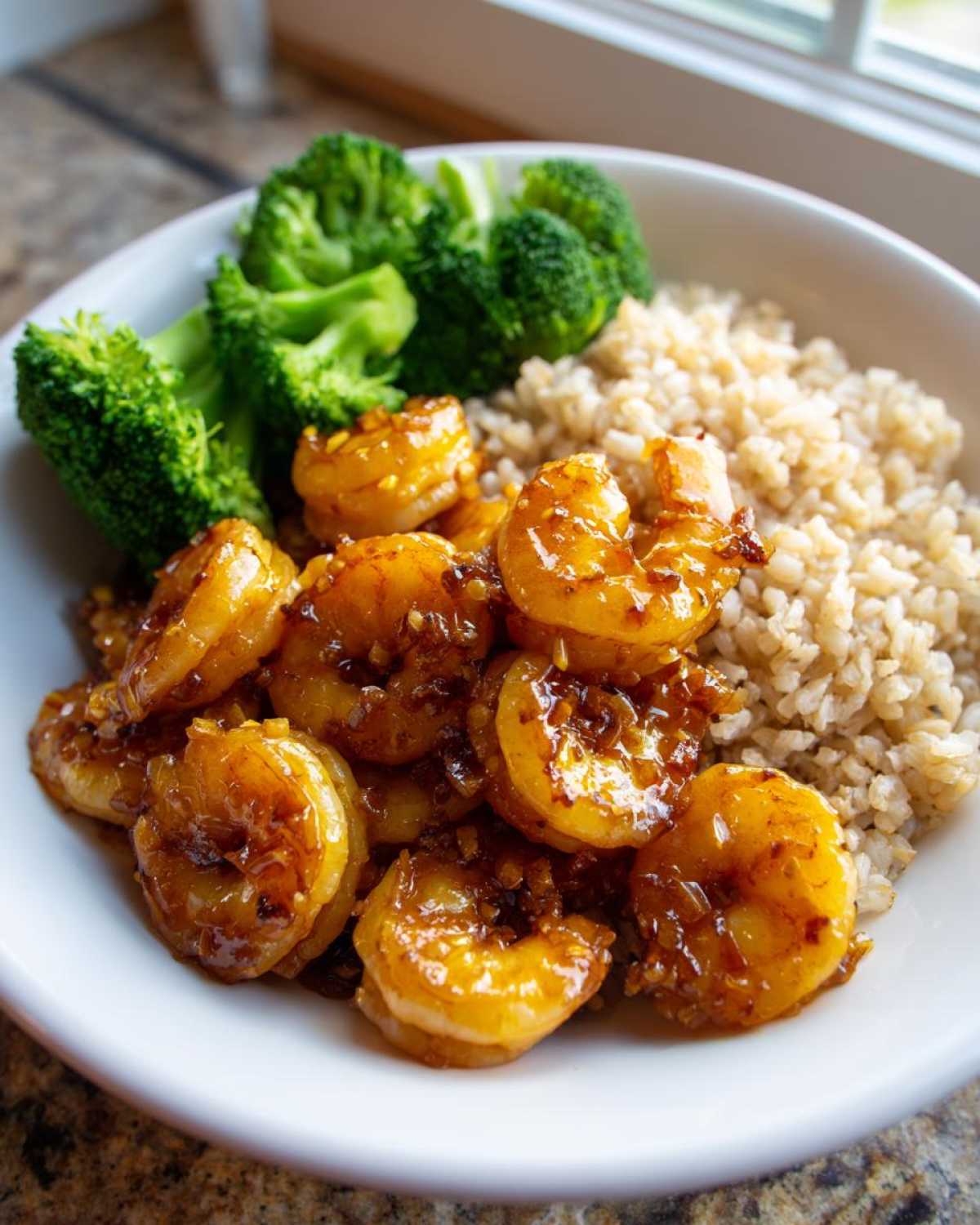 Close-up of a white bowl containing Honey Garlic Shrimp Bowl Quick Dinner with brown rice and steamed broccoli.