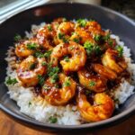 Close-up of glossy Honey Garlic Shrimp Skillet with Rice, topped with fresh parsley in a dark bowl.