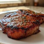 Two thick slices of Honey Glazed Ham Steak in the Skillet, caramelized and glistening with a sweet glaze and herbs.