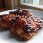 Close-up of three Honey Soy Chicken Thighs with crispy, dark, caramelized edges on a white plate.