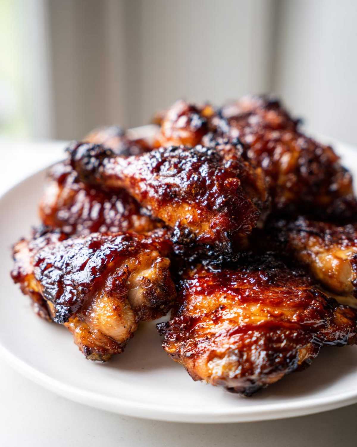A close-up of several glistening Honey Soy Chicken Thighs with crispy, caramelized edges piled on a white plate.
