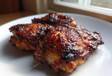 Close-up of three Honey Soy Chicken Thighs with crispy, dark, caramelized edges on a white plate.