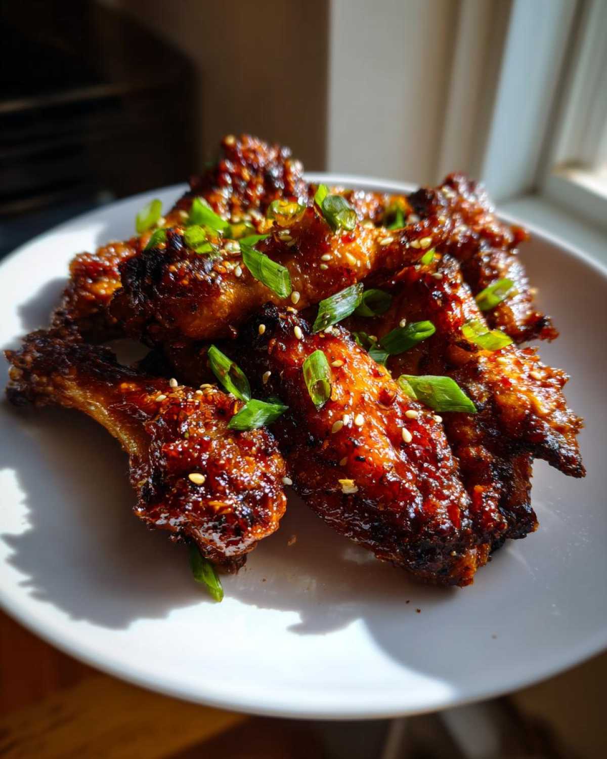A close-up of glossy, dark glazed Honey Soy Chicken Wings Crispy Oven Baked, garnished with sesame seeds and green onions.