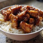 Close-up of crispy chicken pieces coated in glossy sauce served over white rice in a bowl, featuring Honey Soy Garlic Chicken.