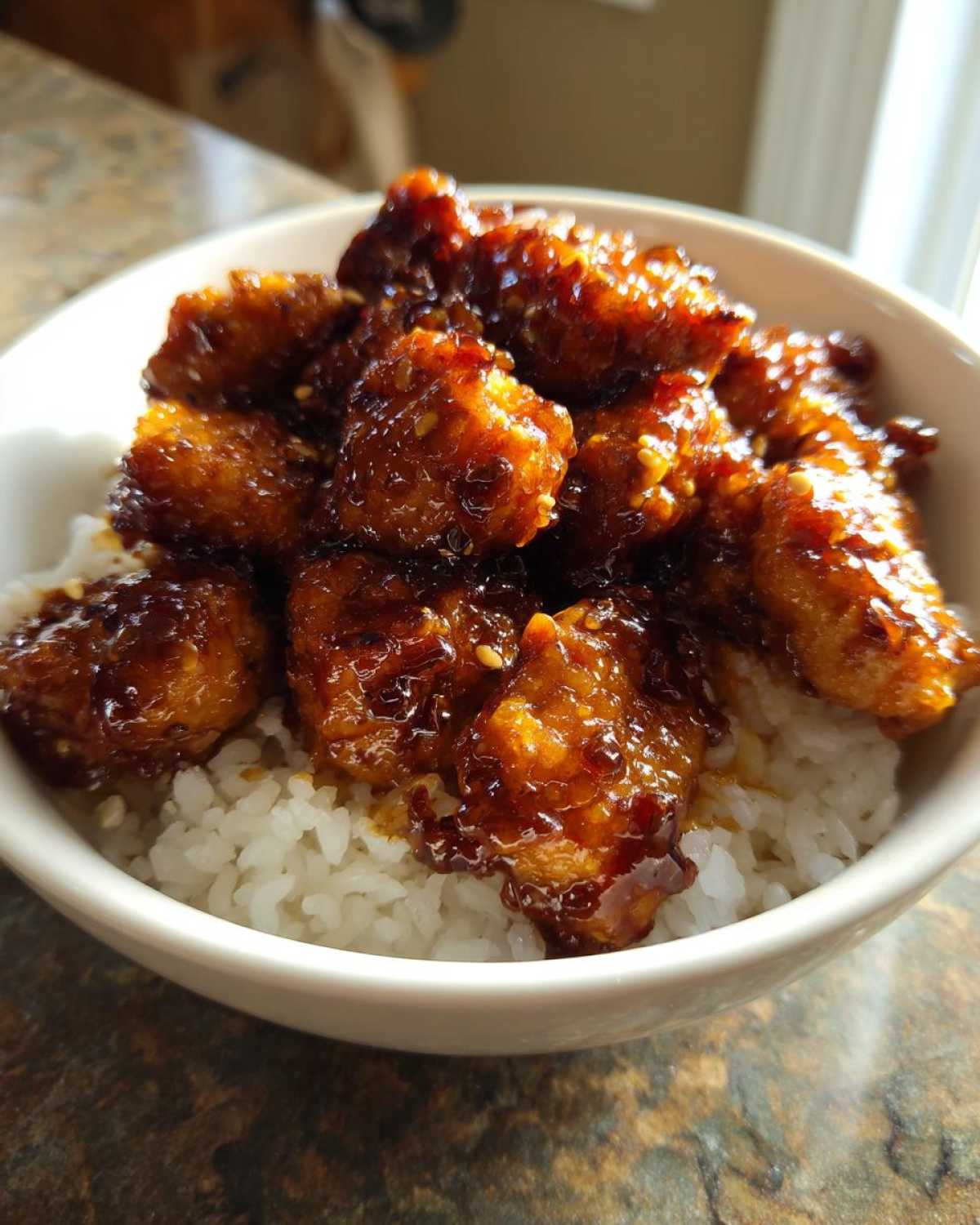 Close-up of crispy Honey Soy Garlic Chicken pieces coated in a thick, shiny glaze served over white rice in a bowl.