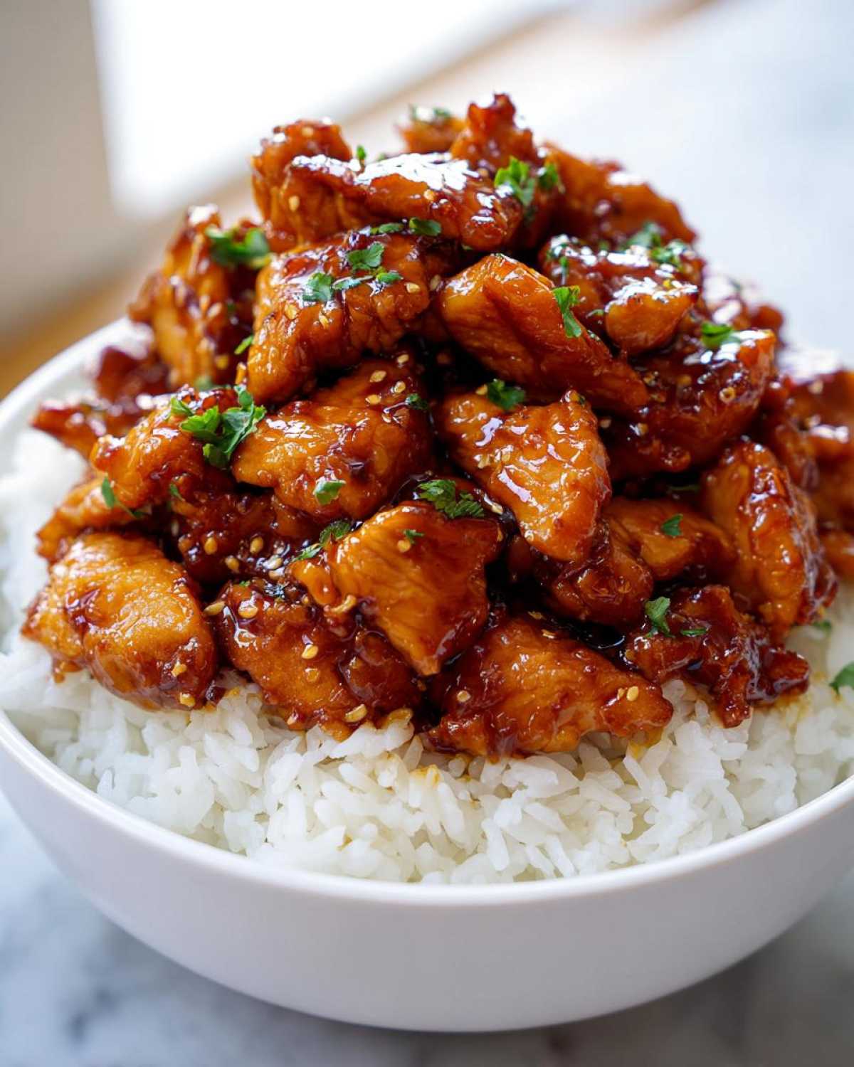 Close-up of Honey Soy Garlic Chicken with rice bowl, topped with sesame seeds and parsley.