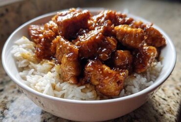 Close-up of crispy chicken pieces coated in glossy sauce served over white rice in a bowl, featuring Honey Soy Garlic Chicken.