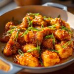 Close-up of crispy, glazed Honey Sriracha Chicken Skillet pieces topped with sesame seeds and green onions.
