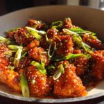 Close-up of glistening Honey Sriracha Chicken Skillet pieces coated in sauce, garnished with sesame seeds and green onions.