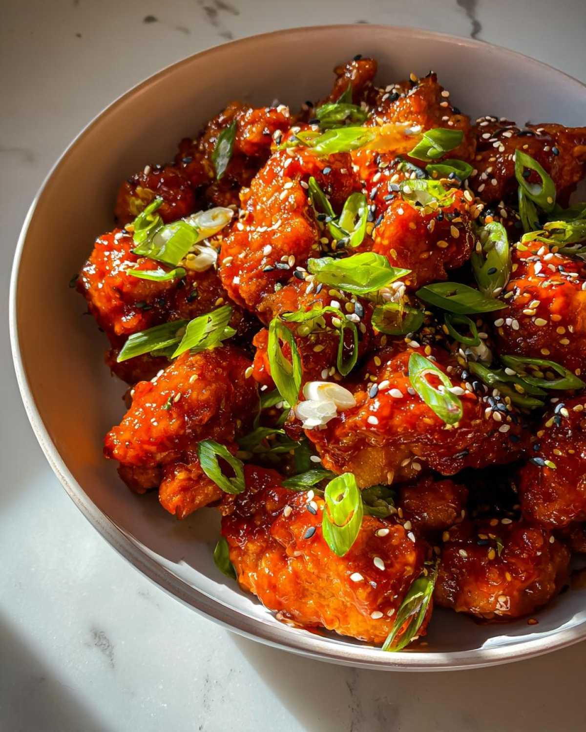 Close-up of glistening Honey Sriracha Chicken Skillet pieces coated in a sweet and spicy glaze, topped with green onions and sesame seeds.