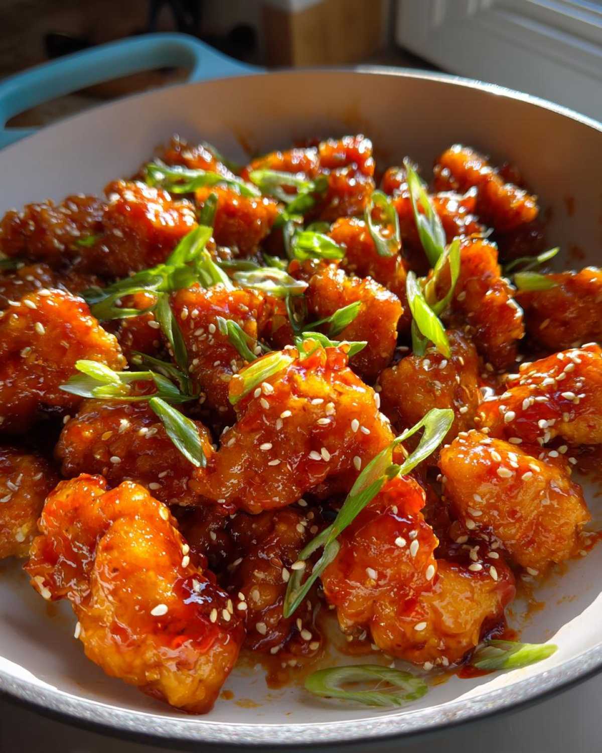 Close-up of crispy chicken pieces coated in a glossy Honey Sriracha Chicken Skillet sauce, garnished with sesame seeds and green onions.