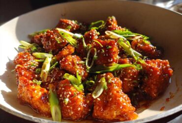 Close-up of glistening Honey Sriracha Chicken Skillet pieces coated in sauce, garnished with sesame seeds and green onions.