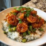 A close-up of a Honey Sriracha Shrimp Bowl featuring glazed shrimp over white rice, garnished with edamame, sesame seeds, and green onions.