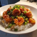 A close-up of a Honey Sriracha Shrimp Bowl featuring glazed shrimp, white rice, edamame, and green onions.