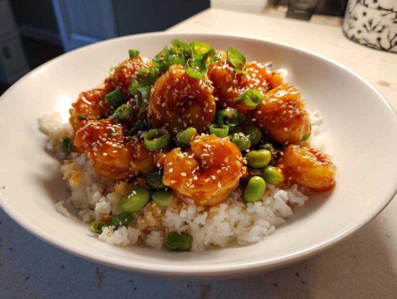 A close-up of a Honey Sriracha Shrimp Bowl featuring glazed shrimp, white rice, edamame, and green onions.