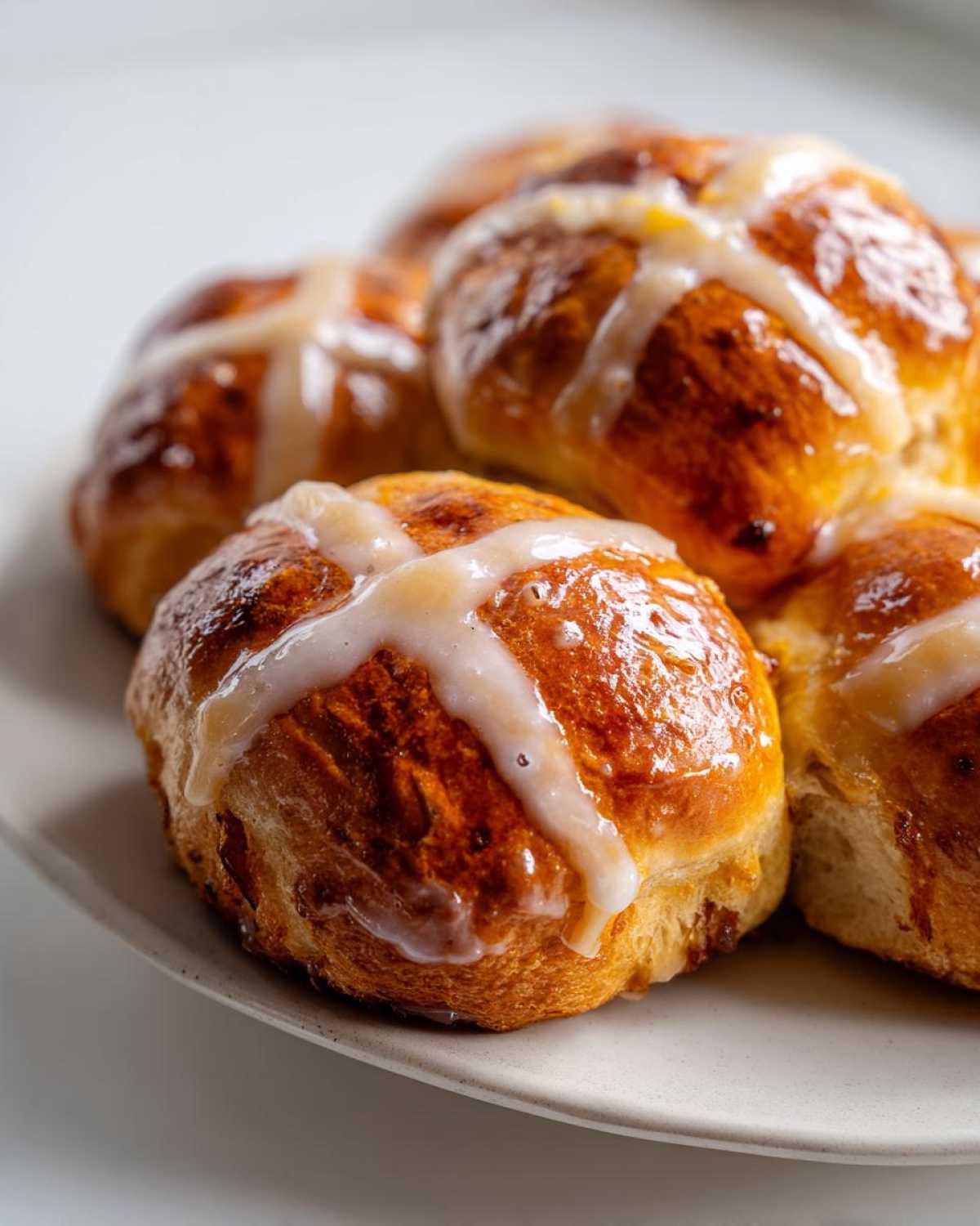 A close-up of several freshly baked Hot Cross Buns with Orange Glaze drizzled across the top.