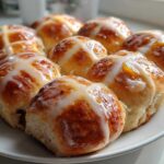 A close-up of freshly baked Hot Cross Buns with Orange Glaze, drizzled with white icing, arranged on a white plate.